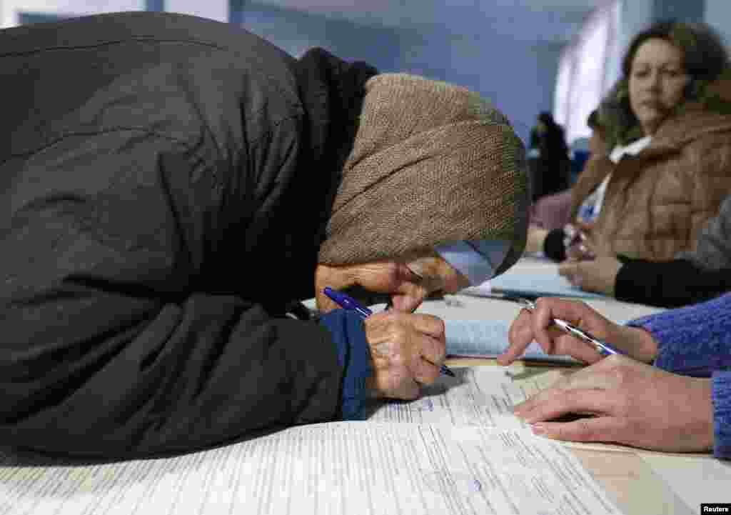 Шығыс Украинадағы Славянск қаласындағы сайлау учаскесіне&nbsp;дауыс беруге келген егде әйел сайлау бюллетенін алғаны туралы құжатқа қол қойып жатыр. 26 қазан&nbsp;2014 жыл. 