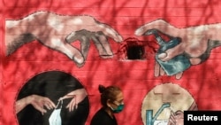 Мумбайлык айым көчөдө сүрөт тартылган дубалдын жанынан өтүүдө. Махараштра штаты, Индия. 2021-жылдын 6-апрели.