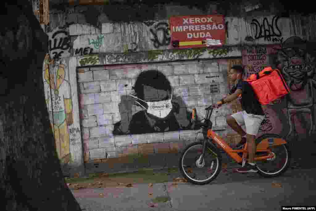 Працівник служби доставки проїжджає повз фреску, на якій зображений президент Бразилії Жаїр Болсонару у захисній масці. Фреска намальована на стіні в центрі міста Ріо-де-Жанейро. Болсонару відкинув ризики, пов’язані з коронавірусом, і кинув виклик пораді міністра охорони здоров’я своєї країни щодо самоізоляції