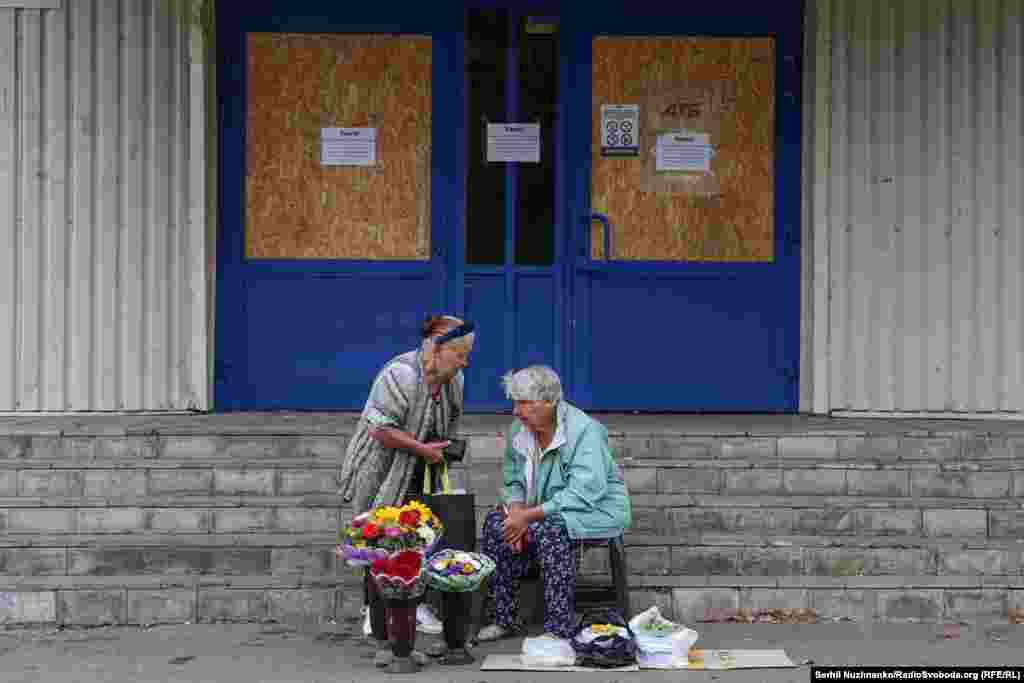 Женщины продают цветы и овощи возле закрытого супермаркета. В городе не работают крупные супермаркеты и торговые центры. Открыты лишь небольшие продуктовые магазины