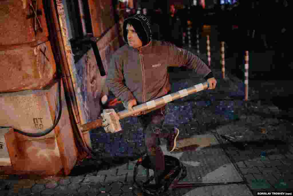 Протестувальник біжить з металевим паркувальним стовпчиком під час демонстрації в Софії, яка переросла в сутички ввечері 1 грудня