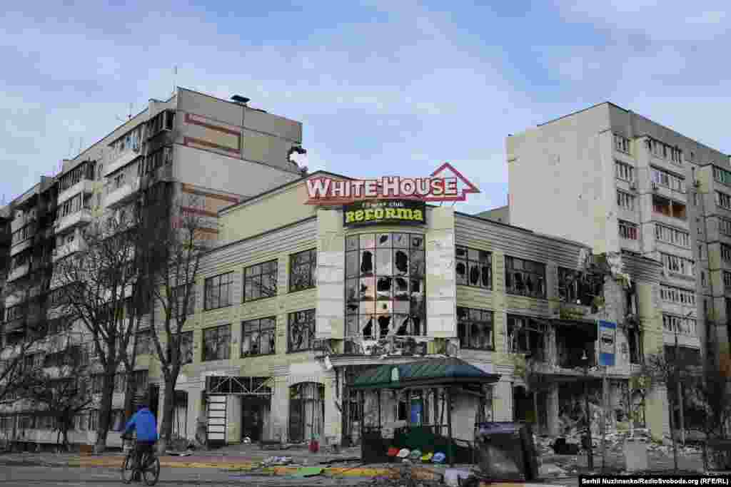 У выніку абстрэлу пацярпеў гандлёвы цэнтар на Гастомельскай шашы. Цяпер гэты будынак адноўлены. Пашкоджаныя абстрэлам жылыя шматпавярховікі ззаду разабралі.Зьлева — фота 7 красавіка 2022 году, справа — з сакавіка 2025 году