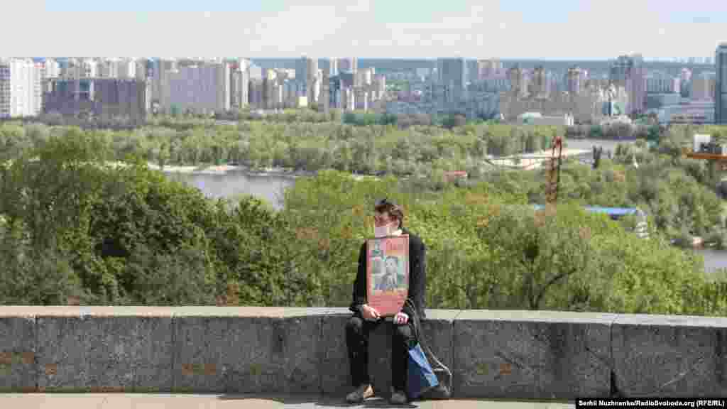 Чоловік у медичній масці та з портретами учасників Другої світової війни сидить у День перемоги біля Вічного вогню у Парку слави. Київ, 9 травня 2020 року БІЛЬШЕ ПРО ЦЕ:&nbsp;9 травня у Києві: квіти, ветерани, Онуфрій, поліція і дезінфекція &ndash; фоторепортаж