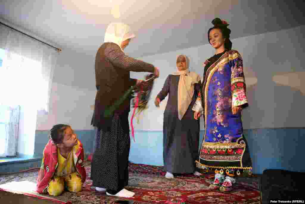 После того, как прическа уложена, девушке помогают одеться. Яркий костюм дунганской невесты состоит из двух рубашек - короткой и длинной, безрукавки, праздничной накидки, штанов, парчовых носков и специальных свадебных туфель. Все компоненты одежды украшены ручной вышивкой.