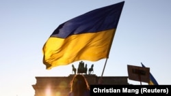 Украинадагы согушка каршы Берлинде өткөн акцияда тартылган сүрөт. Акциянын катышуучусу украин желегин көтөрүп турат. Сүрөт иллюстрация үчүн колдонулду