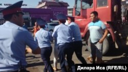 Полиция қызметкерлері орталық базар алдында  сауда орнын бұзуға қарсылық танытқан әйелді әкетіп барады. Шымкент, 30 шілде 2018 жыл. 