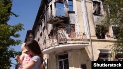 Мама з дитиною біля будівлі в Маріуполі, пошкодженої внаслідок обстрілу в 2015 році