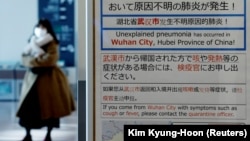 Женщина в маске проходит мимо информационного стенда о вспышке коронавируса в Ухане, Китай, в зоне прилетов аэропорта Ханеда в Токио, Япония. 20 января 2020 года. 