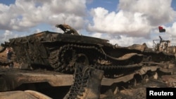 Muammar Kaddafiniň ýaragly güýçlerine degişli tank Bengaziden Ajdabiýah şäherine barýan ýoluň üstünde pytrap ýatyr, 21-nji mart.