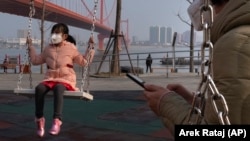 Дівчинка в масці грається біля мосту Ін’ючжоу через річку Янцзи в місті Ухань, 29 січня 2020 року