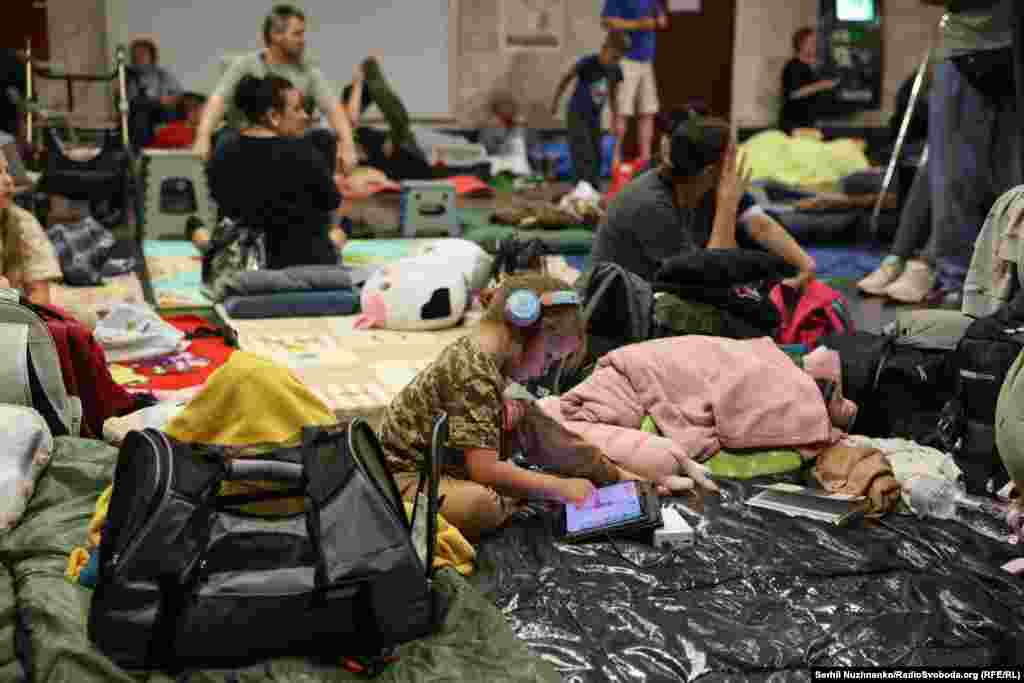 Дзіця ў кіеўскім мэтрапалітэне падчас масаванай расейскай ракетнай атакі. Ліпень 2025 году. Падчас паветраных трывог мэтро ператвараецца ў схоў для тысяч людзей. Паколькі расейская армія мэтанакіравана начамі атакуе ўкраінскую сталіцу, то кіяўляне цэлымі семʼямі сьпяць у мэтро на матрацах, накрыўшыся коўдрамі. Бяруць з сабой хатніх жывёл