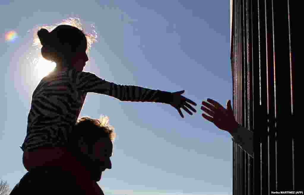 Девочка из Анапры, местности в окрестностях Сьюдад Хуарес в Мексике, пытается дотянуться до руки человека за ограждением, находящимся на территории США. В это же время священники двух стран 26 февраля вознесли молитвы за мигрантов и людей, живущих в этой приграничной зоне. Забор является одним из нескольких барьеров на границе, которые администрация президента США Дональда Трампа планирует расширить, возведя основательную высокую стену.