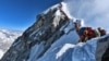 heavy traffic of mountain climbers lining up to stand at the summit of Mount Everest