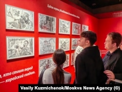 Посетители рассматривают пропагандистские зарисовки, изображающие северокорейских солдат, сражающихся против украинцев