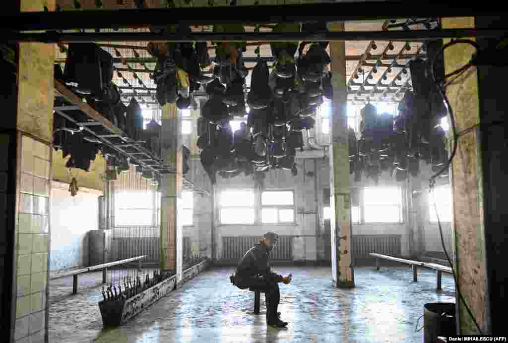 Work clothes hang from the ceiling above a miner in the locker room.&nbsp;