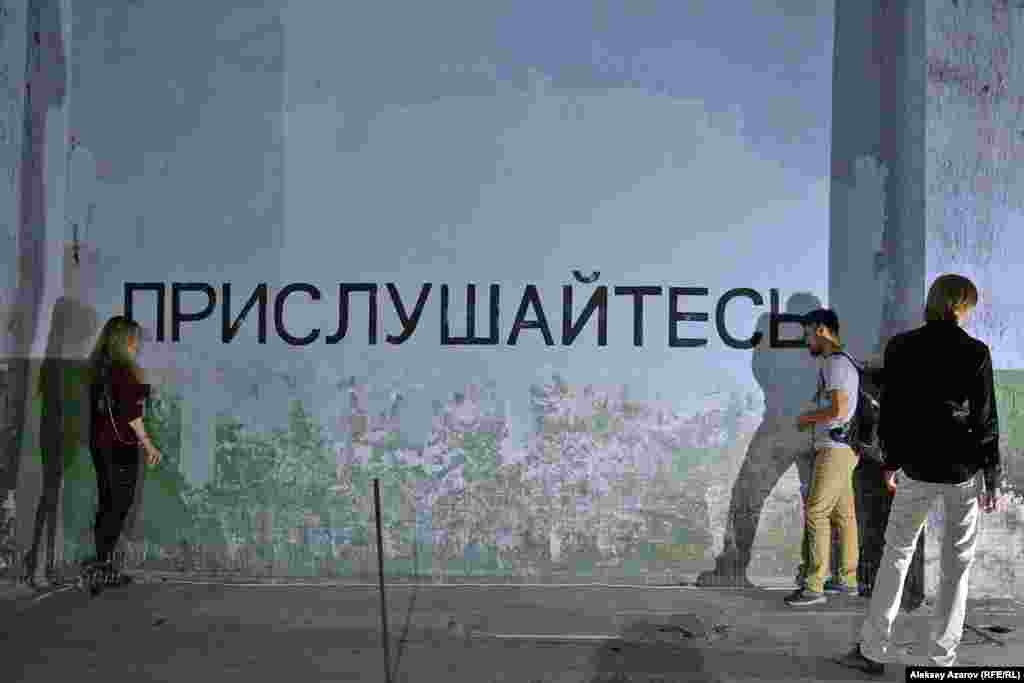 Девушка, обозначенная в каталоге выставки как Мира Евгеньевна,&nbsp;создала инсталляцию из надписи на стене: &laquo;Прислушайтесь&raquo;, динамиков и аудиозаписей. Если приложить ухо к динамикам, то с одной стороны слышны сводки новостей нашего времени, а с другой стороны&nbsp;&mdash; записи выступлений деятелей партии &laquo;Алаш&raquo;, &laquo;Алаш-Орды&raquo;. Эта инсталляция&nbsp;&mdash; плод размышления о &laquo;деградации современного человека&raquo;, о людях, не образованных как умственно, так и эстетически.&nbsp;