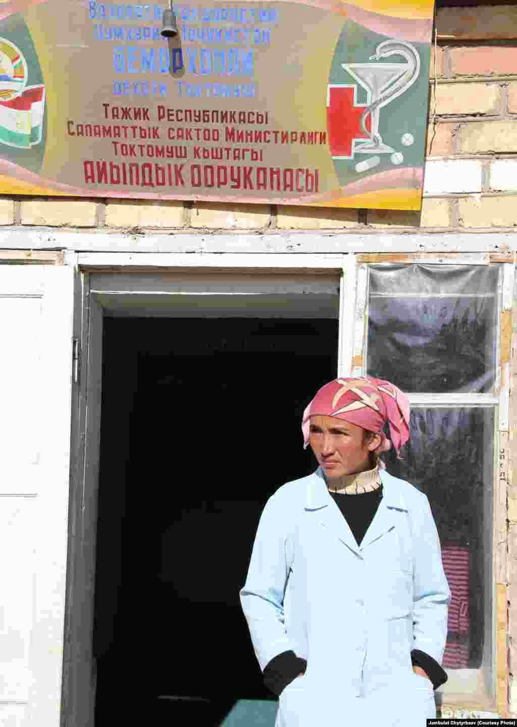 Сүрөттө: Медициналык кызматкер айылдык оорукананын алдында турат, Токтомуш айылы, Мургаб району. Акыркы жылдары Мургабдагы аталыштар, жарнамалар тажикче жазыла баштады, бирок Токтомуш айылында жазуулар эки тилде жазылат. Активисттер район жетекчилиги далалаттанса, бардык жазууларды эки тилде сактап калууга болот эле дешет.