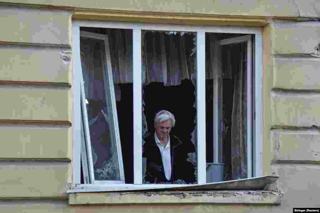 Мешканець пошкодженого будинку у Львові, прибирає уламки скла розбитого вікна через атаку РФ